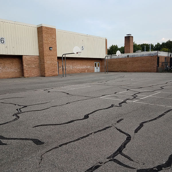 cracks with tar on asphalt with basketball court at school